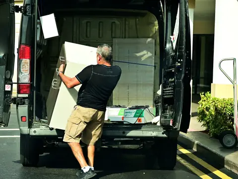 A man loading a large box into the back of a van on a sunny street