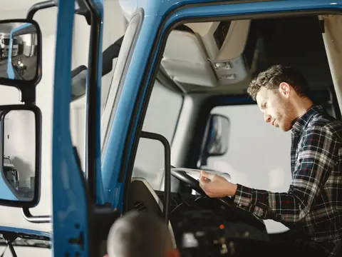 A man checking a tablet in the cab of a blue truck