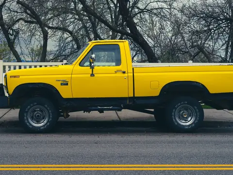A yellow pickup truck parked on a sunny street beside a white fence