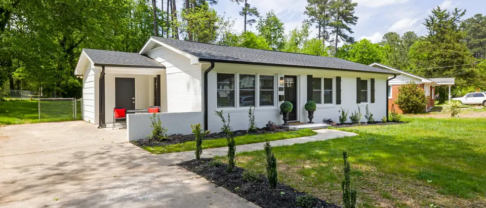 A white single-story house with a long driveway and a green lawn