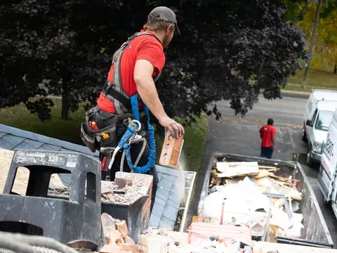 A worker in a safety harness loading broken building debris into a truck bed