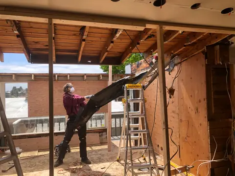 A man pulling down old wood boards from a timber frame under open sky