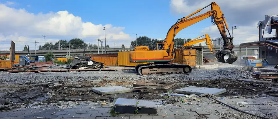 An excavator on a cleared demolition site under a bright sky