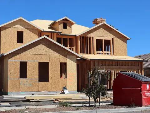 A red roll-off container beside a new house under construction on a sunny day