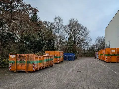 Orange roll-off containers lined up along a paved yard road