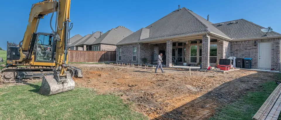 An excavator at work beside a new brick house under a blue sky