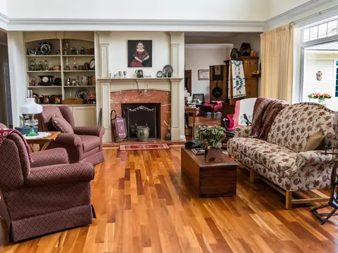 A furnished living room with a brick fireplace, armchairs and a floral sofa on a wood floor