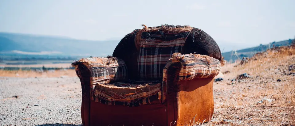 A worn armchair standing alone in a dry field under a blue sky
