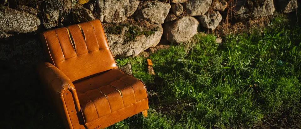 An orange leather armchair left on the grass beside a stone wall