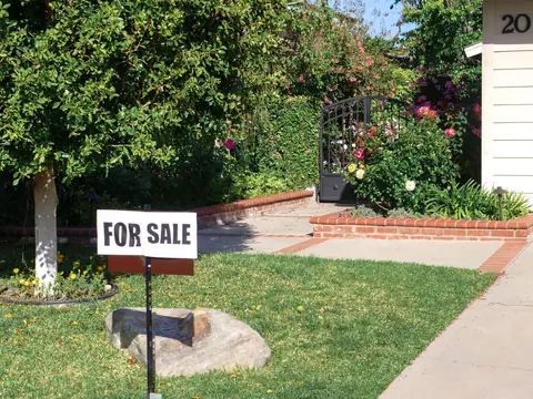 A small sign in a front yard beside a driveway and a garage