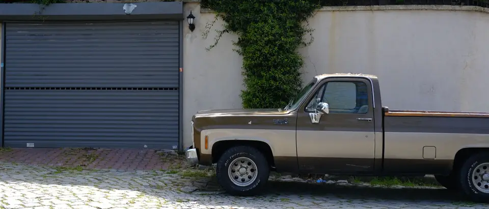A brown pickup parked in front of a garage on a sunny paved drive