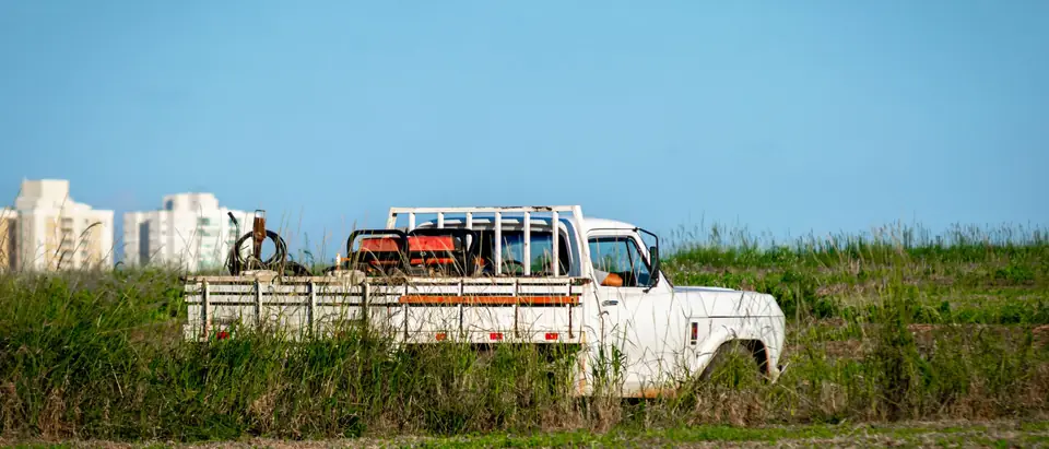 A white pickup loaded with scrap parked in tall grass
