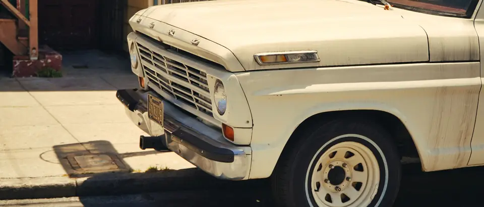 The front of a cream vintage pickup truck parked on a sunny street
