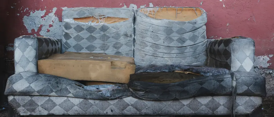 An old, worn sofa left against a pink wall