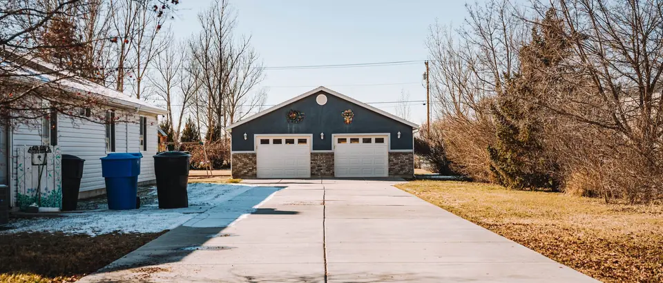 A long driveway leading to a two-door garage, trash bins at its side