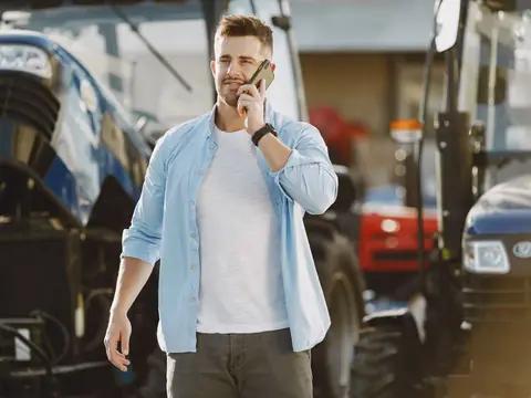 A man taking a phone call as he walks through a yard of parked trucks and tractors