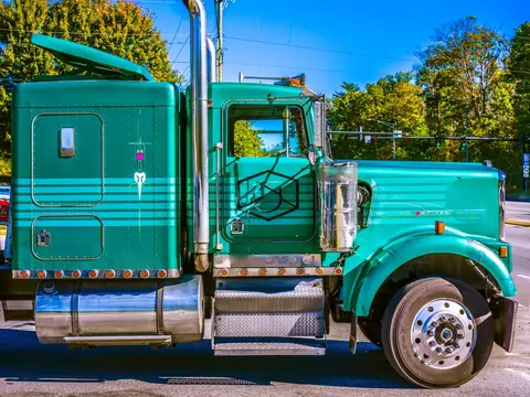 A green semi truck cab parked in the sun, seen from the side