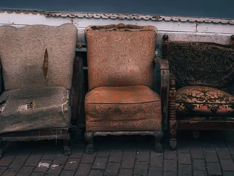 Three worn armchairs lined up against a wall on a paved sidewalk