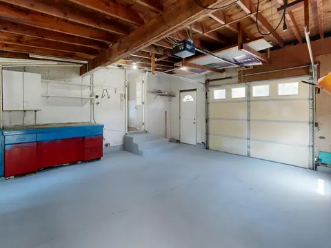 An empty garage with a roll-up door, cabinets and a clean gray floor