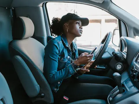 A woman in the driver's seat of a van looking up from her phone