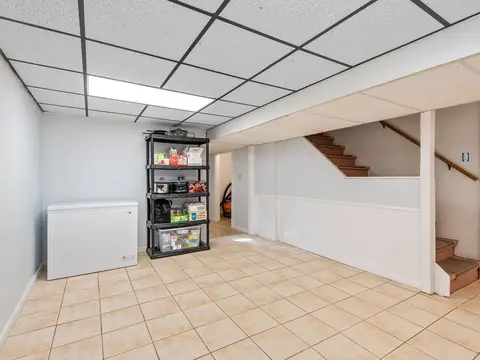 A bright, cleared basement with a tiled floor, a freezer and a stairway
